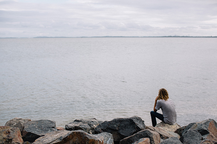 Lone person sat atop ocean-side rocks
