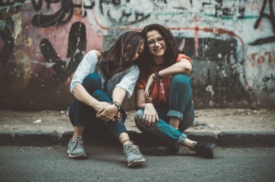 Two friends leaning together on pavement